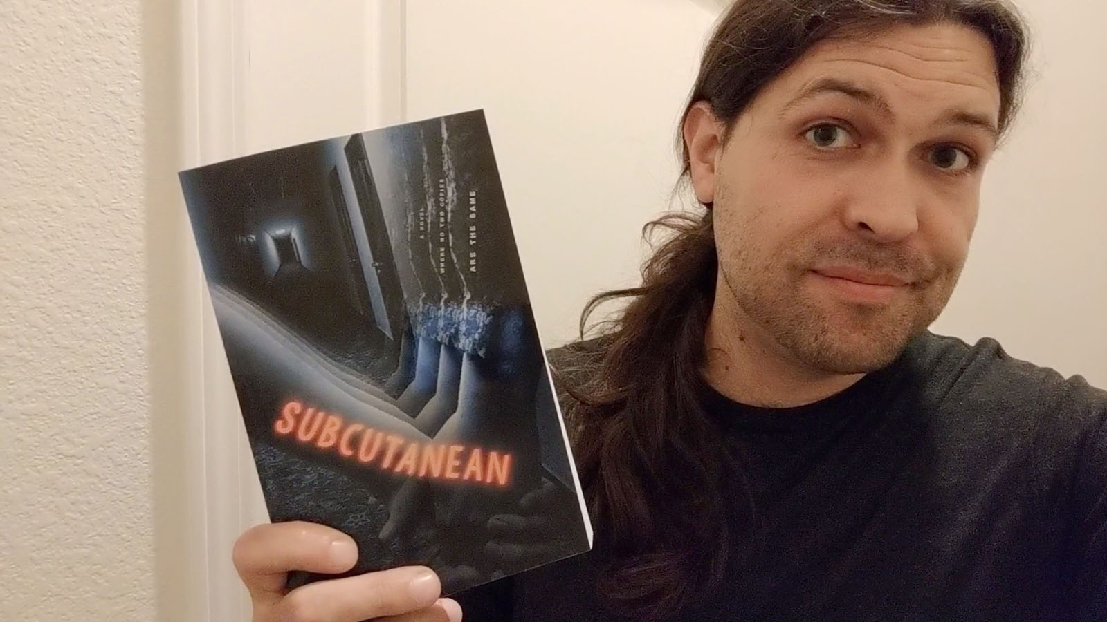 Photo of author Aaron A. Reed in 2020, holding a paperback copy of Subcutanean.